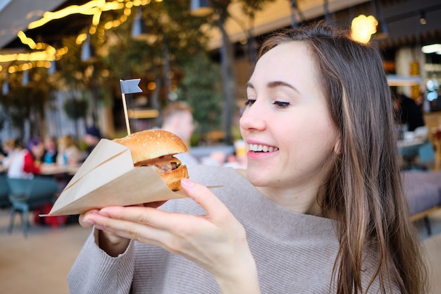 La ragazza tiene in mano un hamburger e lo guarda.