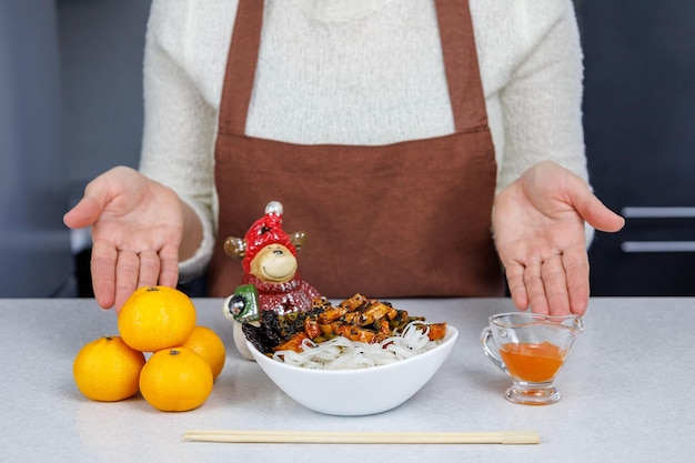 La ragazza tiene in mano un piatto di spaghetti di riso e pollo Mandarini sul tavolo Sfondo scuro della cucina di casa