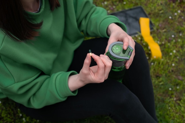 La ragazza tiene in mano vitamine e una bottiglia la primavera nella foresta vestita con una giacca verde