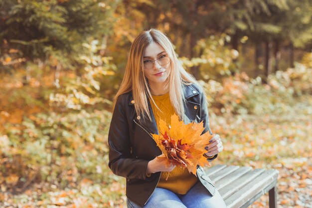 La ragazza tiene le foglie cadute nel parco autunnale. Concetto stagionale.