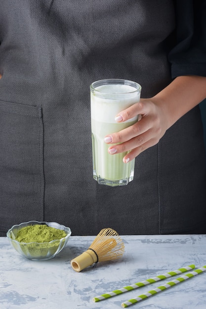 La ragazza tiene tra le mani un bicchiere con una bevanda salutare con latte di gufo. Tè verde matcha latte. Prodotto vegetariano