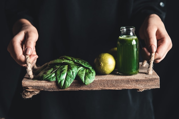 La ragazza tiene tra le mani un vassoio vintage con frullato di spinaci, lime e spinaci. Cibo sano, eco, vegano.