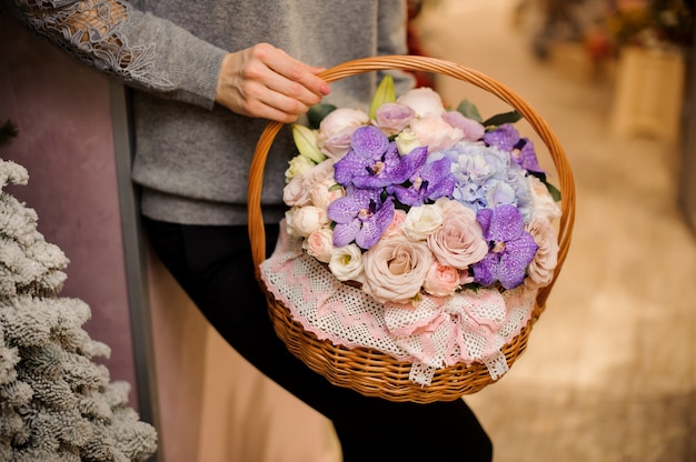 La ragazza tiene un cesto con orchidee viola, rose rosa e ortensia blu