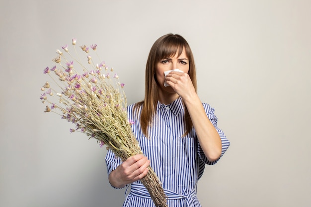 La ragazza tiene un mazzo di fiori di campo su uno sfondo chiaro che soffre un'allergia ai fiori