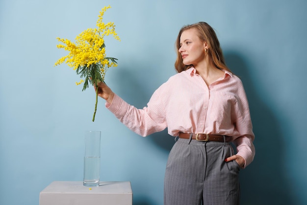 la ragazza tiene un ramo di mimosa in mano e lo mette nel concetto di sorgente d'acqua