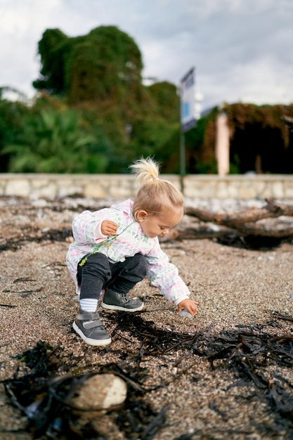 La ragazzina si accovaccia sulla spiaggia e tocca una pietra con la mano.