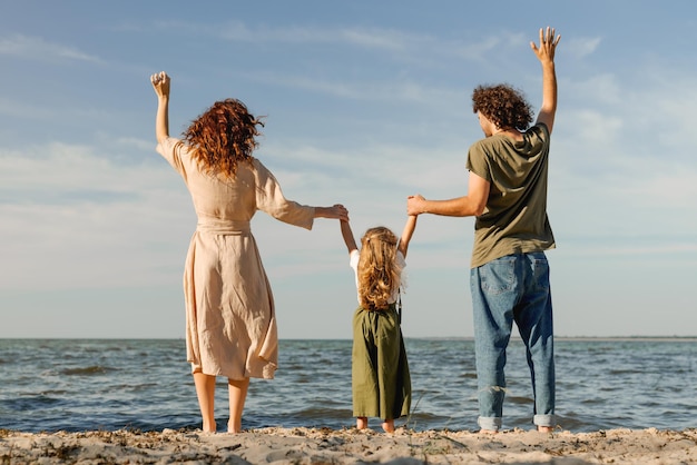 La retrovisione del padre felice, la madre e la piccola figlia stanno sulla riva del mare in una giornata di sole