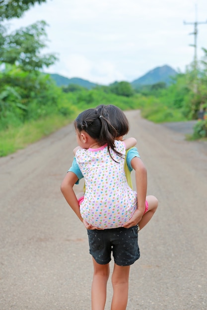 La retrovisione di giovani ragazza asiatica e sua sorella guidano indietro e camminando sulla strada campestre.