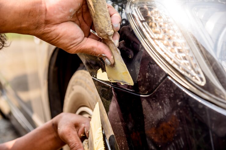 La riparazione del riparatore del lavoratore meccanico ha graffiato sulla carrozzeria e sta preparando per dipingere.