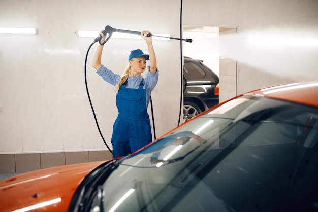 La rondella femminile in uniforme pulisce l'auto con la pistola ad alta pressione nelle mani