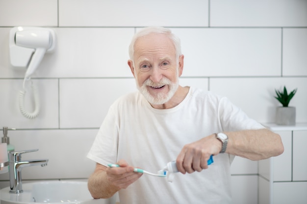 La routine mattutina. Uomo in maglietta bianca che fa le procedure mattutine in un bagno