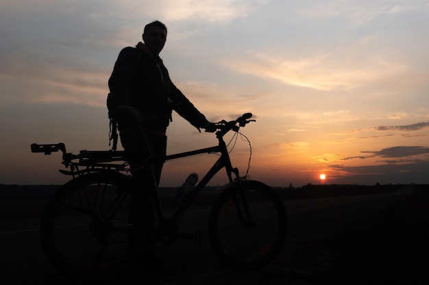 La sagoma di un ciclista sullo sfondo del sole e il bel cielo La sagoma di un uomo in piedi accanto alla sua bicicletta sullo sfondo del tramonto