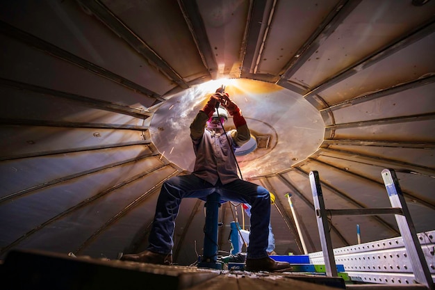 La saldatura ad arco metallico del lavoratore di sesso maschile fa parte della costruzione di serbatoi sul tetto di serbatoi di stoccaggio di petrolio e gas all'interno di spazi ristretti