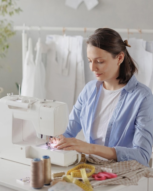 La sarta della donna del primo piano in officina cuce i vestiti per la vendita sul posto di lavoro accogliente piccola impresa o hobby