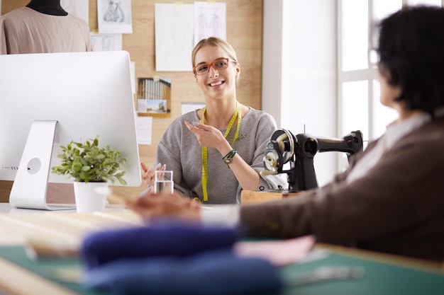 La sarta femminile sta comunicando con il potenziale cliente in merito all'abito su misura nel laboratorio di cucito