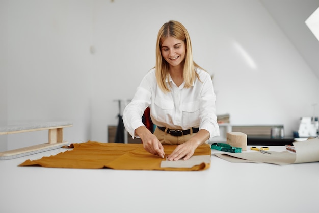 La sarta lavora con il modello di stoffa sul posto di lavoro in officina. Occupazione sartoriale e cucito professionale, attività di sartoria artigianale, hobby artigianale