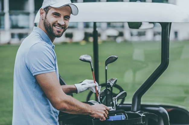 La scelta del driver corretto. Bel giovane giocatore di golf maschio che sceglie autista mentre si trova vicino al carrello da golf