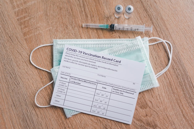 La scheda di registrazione della vaccinazione contro il coronavirus è posizionata su un pavimento di legno con una siringa per vaccino