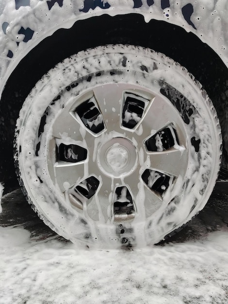 La schiuma bianca scorre lungo la ruota dell'auto e il cappuccio sull'asfalto dell'autolavaggio