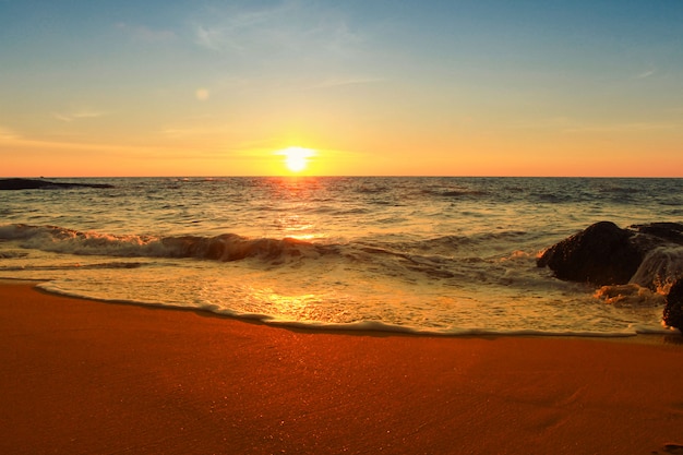 La schiuma molle del mare ondeggia la spiaggia in un tempo dorato del tramonto sull'oceano del Pacifico meridionale con le riflessioni variopinte e il backgound del cielo