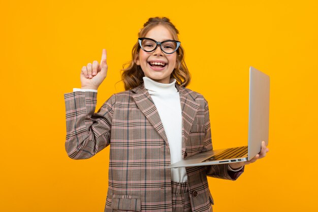 La scolara caucasica astuta divertente con gli occhiali in un vestito e una giacca con un computer portatile in mano spiega la teoria sull'arancia