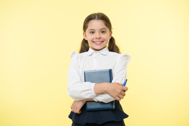 La scolara ha letto il libro isolato su bianco. Il piccolo bambino con i capelli lunghi tiene il libro di testo con la penna. Dedicato allo studio. Adorabile topo di biblioteca. Di nuovo a scuola.