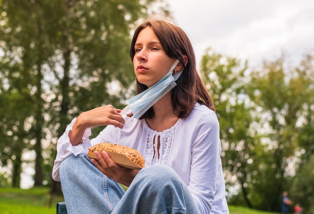 La scolara in una maschera medica mangia un panino in natura