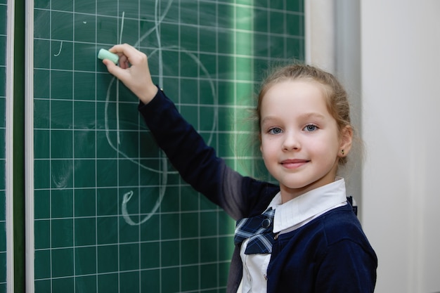 La scolara in uniforme scrive con il gesso su una lavagna. Istruzione primaria scolastica. Messa a fuoco selettiva.