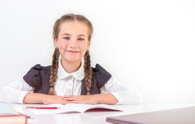 La scolara si siede dietro un banco di scuola e sorride su uno sfondo bianco