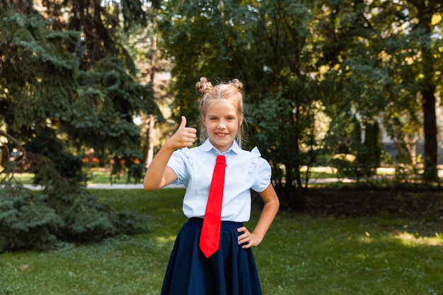 La scolaretta della bambina mostra un gesto di approvazione della classe con due mani mentre cammina nel parco.