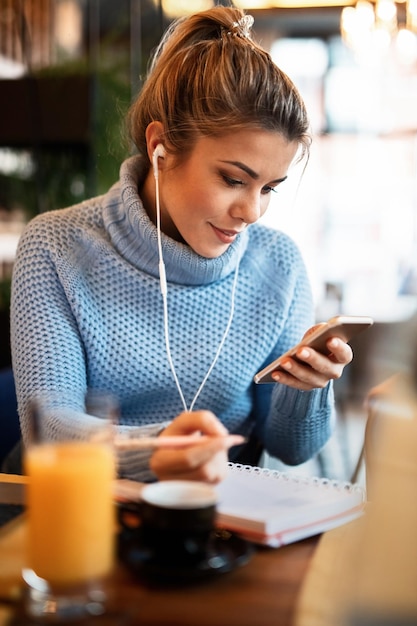 La scrittura freelance femminile sorridente fa per elencare nel suo pianificatore settimanale mentre utilizza il telefono cellulare nella caffetteria