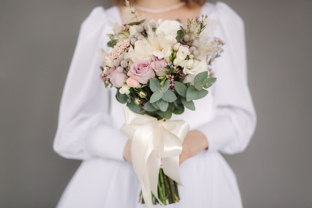 La selezione centrale della sposa tiene il bouquet da sposa nelle mani sfondo grigio studio fotografico