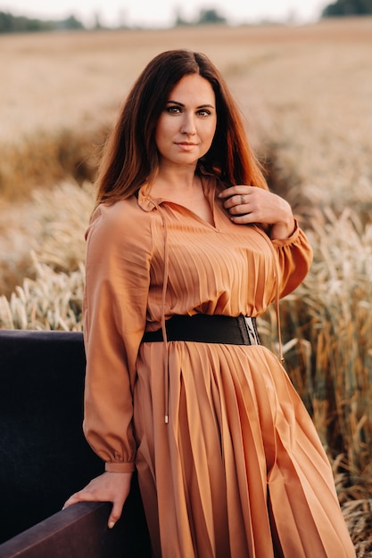 La sera una ragazza con un vestito arancione sta accanto a una sedia in un campo di grano