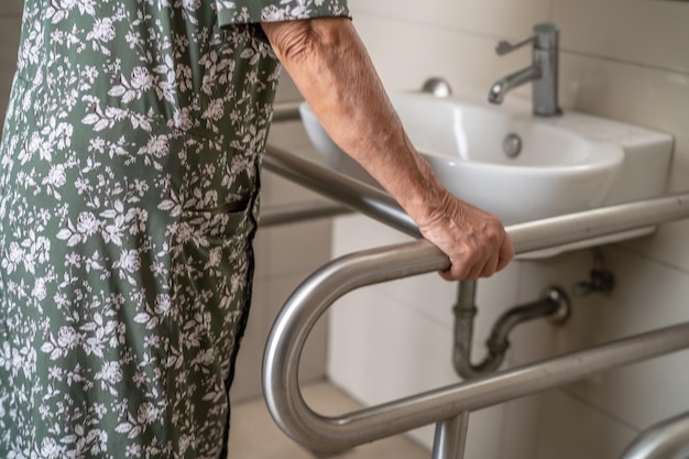 La sicurezza della maniglia del bagno della toilette di uso del paziente della donna anziana asiatica nel concetto medico forte sano dell'ospedale di cura