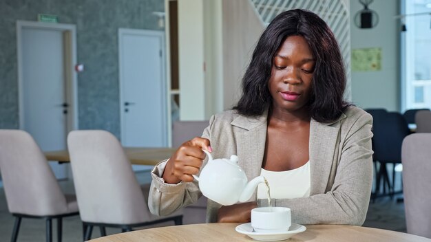 La signora afroamericana versa l'acqua calda nella tazza nell'accogliente caffè