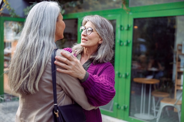 La signora anziana positiva abbraccia l'amico con i capelli grigi che si incontrano sulla strada della città