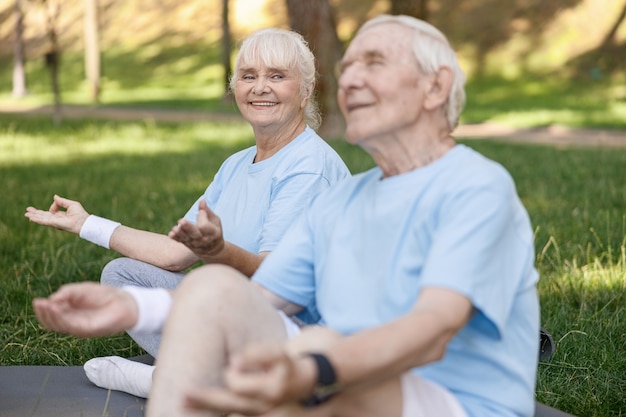 La signora anziana sorridente guarda il partner rilassato che medita insieme nel parco