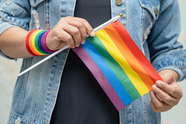 La signora asiatica che indossa una giacca di jeans blu o una camicia di jeans e tiene in mano una bandiera color arcobaleno, simbolo del mese dell'orgoglio LGBT celebra annualmente a giugno sociale di gay, lesbiche, bisessuali, transgender, diritti umani.