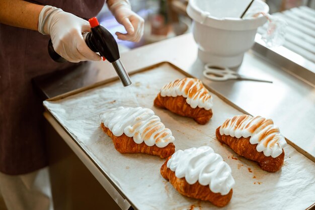 La signora brucia la crema all'albume che decora i croissant freschi nel negozio di panetteria