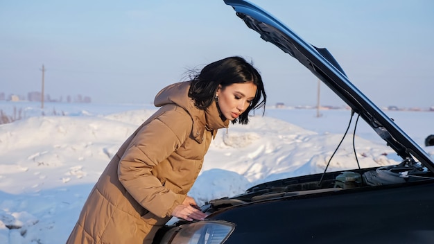 La signora guarda il motore dell'automobile rotta sulla strada innevata