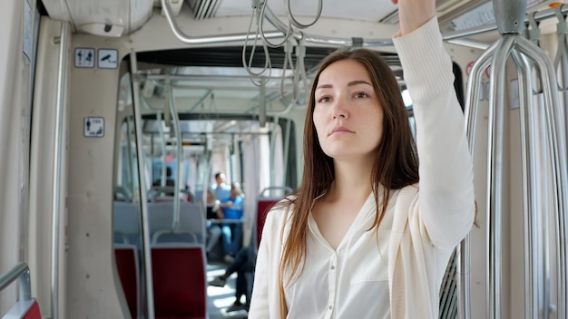 La signora premurosa in abiti bianchi si trova nel vagone del tram e tiene la fasciatura del corrimano che viaggia verso il centro città primo piano