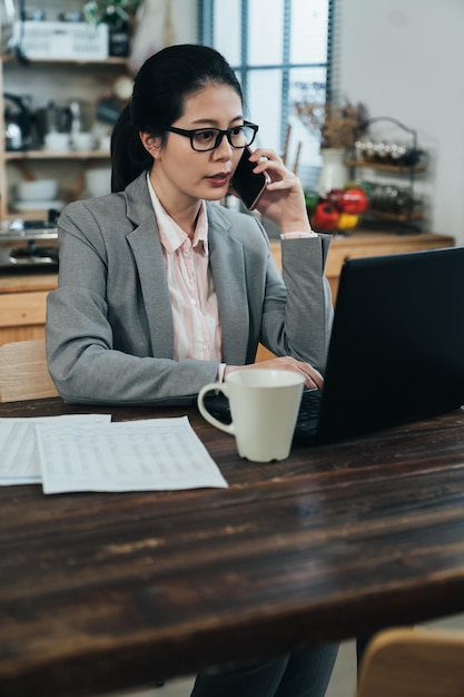 la signora professionista giapponese che guarda lo schermo sta confermando i dettagli con il collega al telefono. la seduta del manager femminile asiatico sta comunicando con i clienti con il cellulare e controllando i piani sul computer.