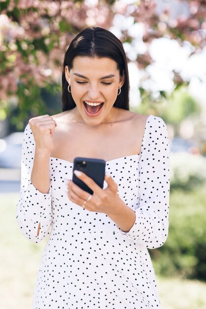 La signora sorpresa che celebra la vittoria al telefono il ritratto della donna felice gode del successo sul telefono cellulare