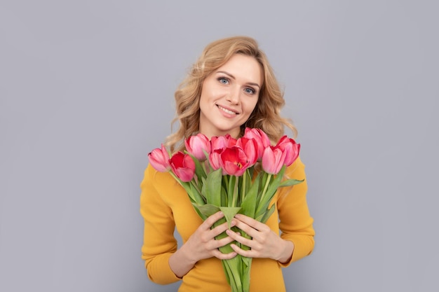 La signora sorridente tiene i fiori per le vacanze primaverili su sfondo grigio