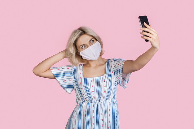 la signora sta facendo un selfie su un muro rosa mentre indossa una maschera