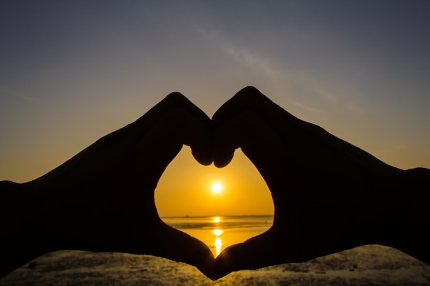 La silhouette della mano di un uomo in una bellissima alba cattura il sole nel cuore.