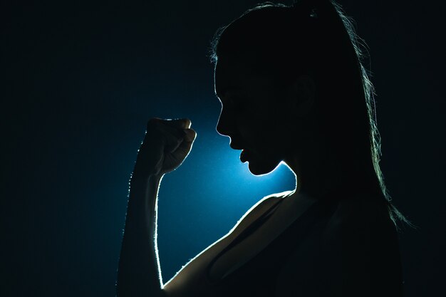 La silhouette della ragazza fitness in piedi nella stanza buia