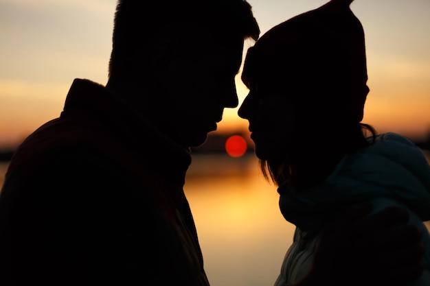 La siluetta degli amanti si accoppia al tramonto in riva al lago sole tra i profili delle persone sull'acqua del cielo al tramonto