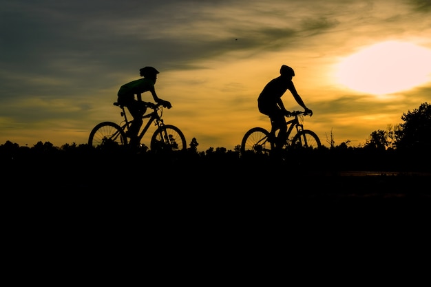 La siluetta degli uomini delle coppie guida le biciclette al tramonto.