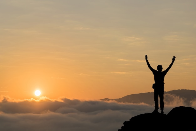 La siluetta dell&#39;uomo sostiene le mani sul picco della montagna, concetto di successo